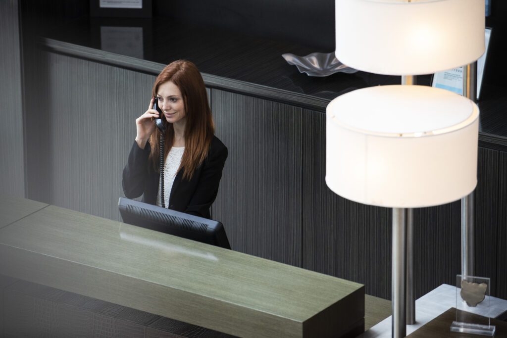 Smiling female receptionist talking on telephone while standing at hotel reception