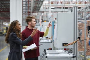 Des ingénieurs hommes et femmes discutent devant le panneau de contrôle. Le directeur et l'ouvrier font des gestes dans une usine automobile. Ils tiennent des documents et une tablette numérique dans l'industrie.