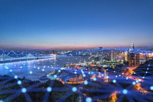 Landscape image of a ciry with a hanging bridge. Superimposed on this image are light blue interconnected dots.