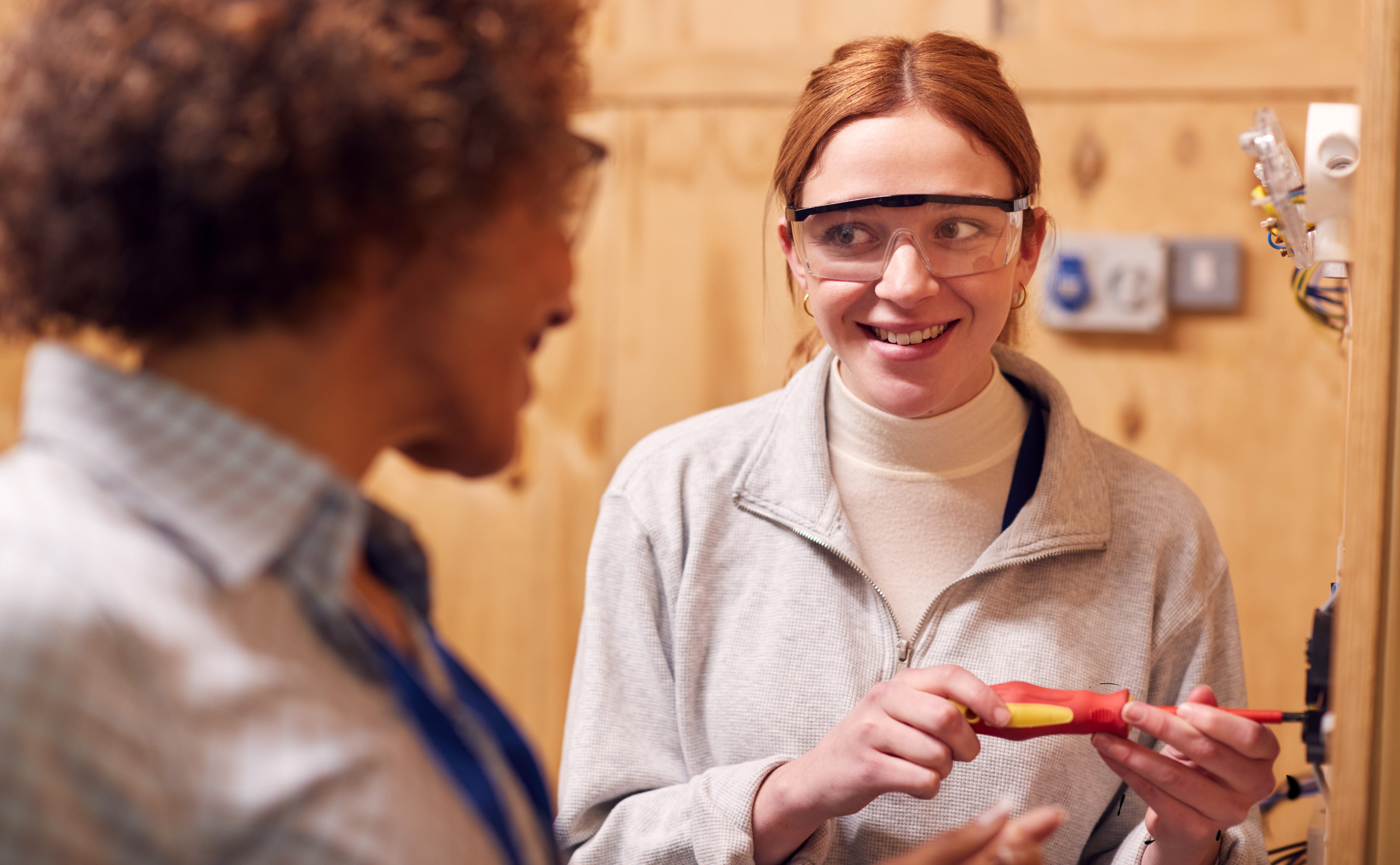 Female Tutor With Trainee Electrician In Workshop Studying For Apprenticeship At College