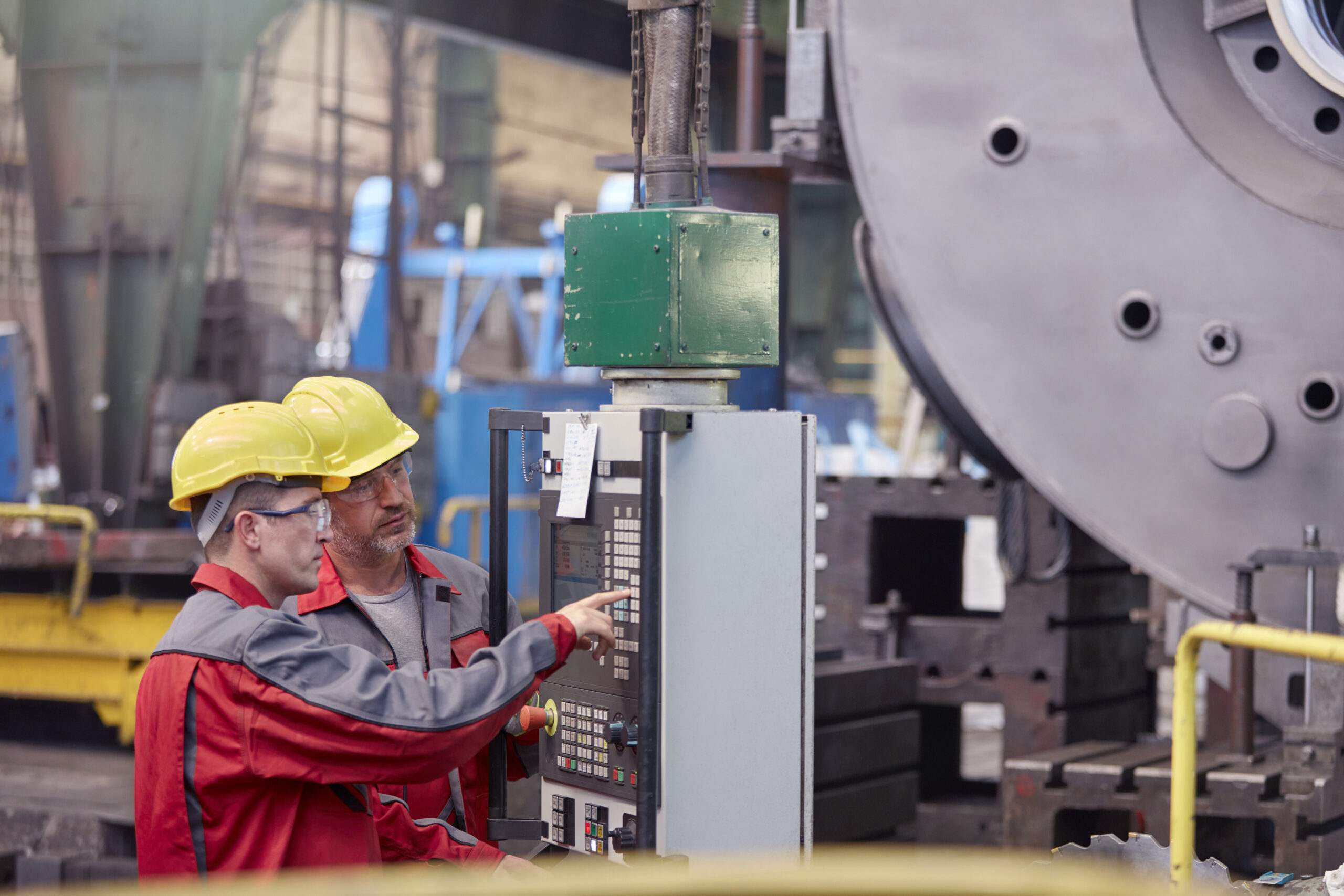 Male workers operating machinery at control panel in factory