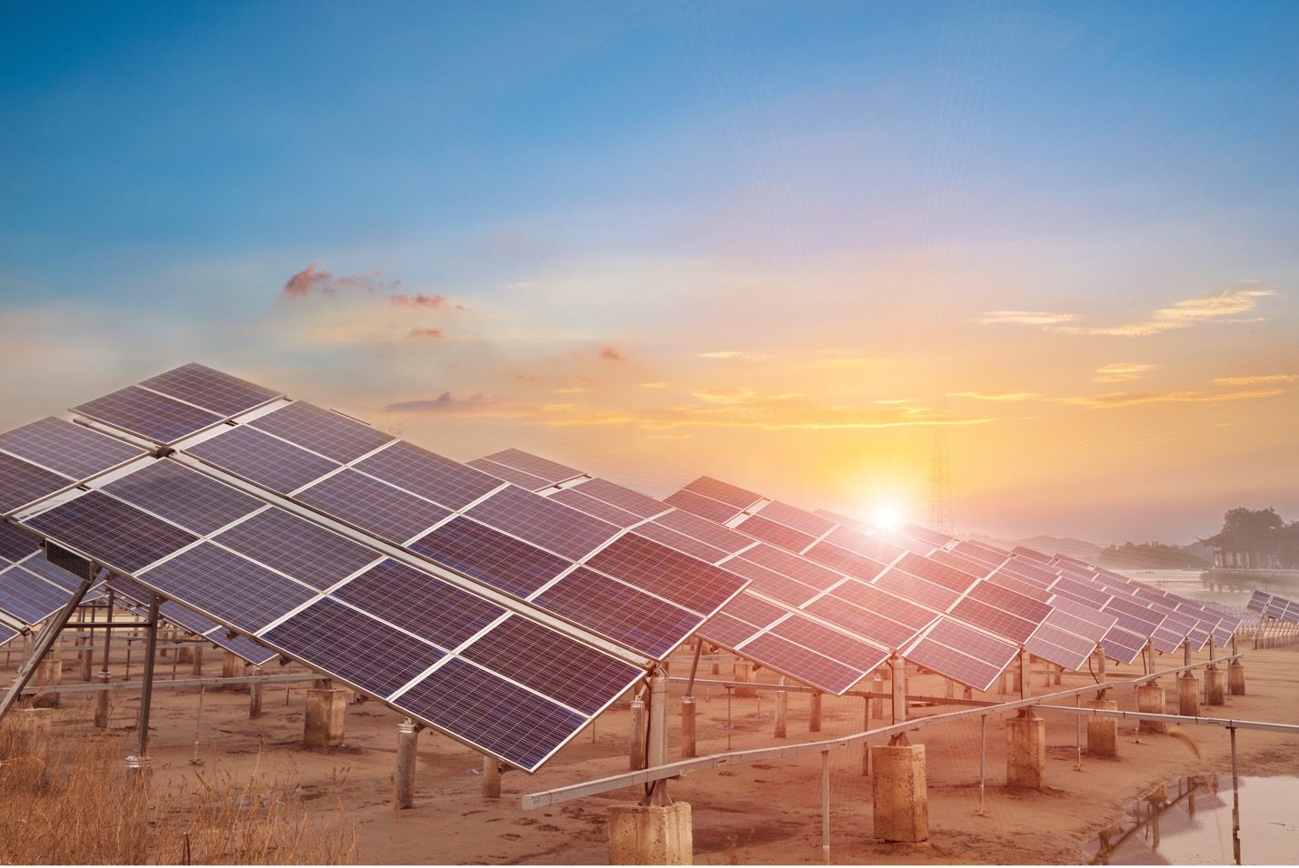 A field of solar photovoltaic (PV) panels with a setting sun in the background.