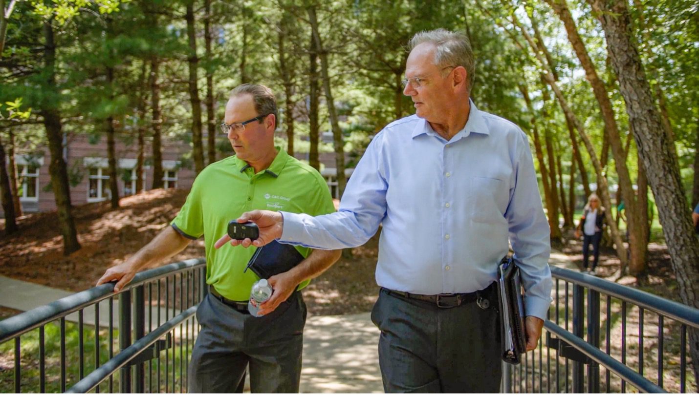 EcoXpert Danny Davies and a colleague walk across a bridge on the wooded Aspiria campus.