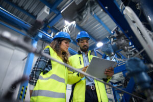 Two engineers wearing PPE control machinery with a large tablet.