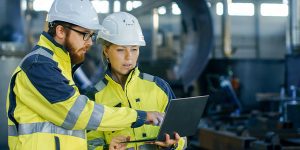 Two engineers in high-visibility jackets and safety helmets using a laptop for Digital Asset Tracking in an industrial setting