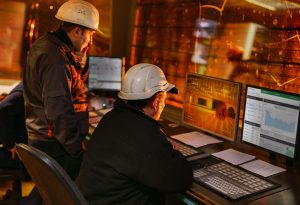 Operators monitor glass production on control screens.