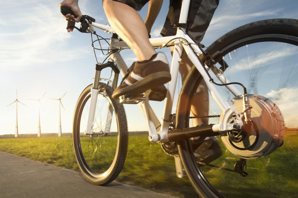 Low angle photo of an adult riding an electric bicycle with wind turbines in the background.