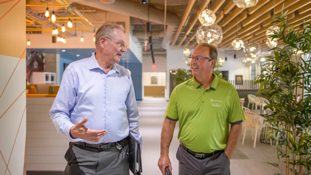 Two men, one in a blue button down shirt and one in a lime green polo shirt,  walk through a building on the Aspiria business campus