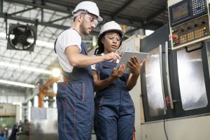 Two workers in overalls look at a data on a tablet in a factory.