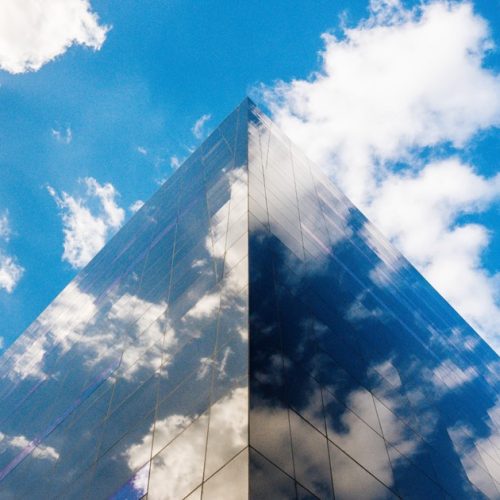 Modern glass office building with cloud landscape to abstractly represent the cloud computing landscape.