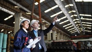 Factory manager or businessman and female engineer in factory. elegant man inspecting factory safety in industry plant background.