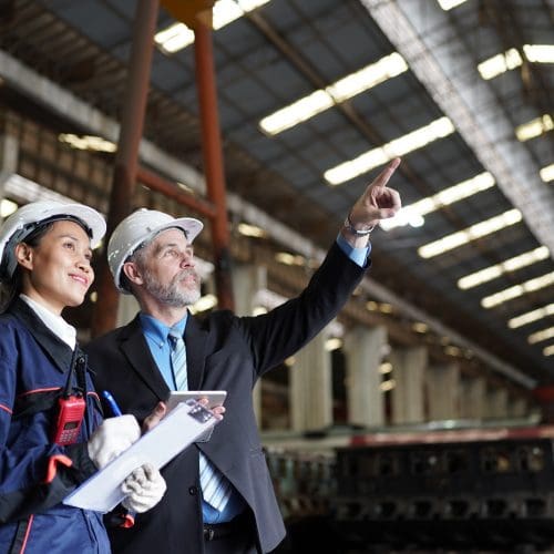 Factory manager or businessman and female engineer in factory. elegant man inspecting factory safety in industry plant background.