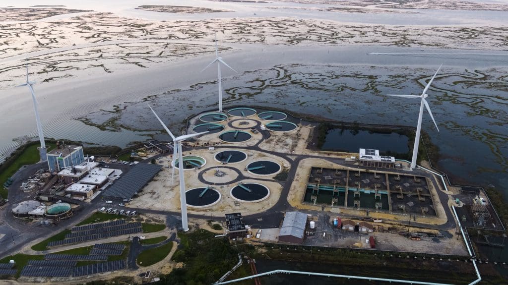 Sustainable energy is used in environmental conservancy. A wastewater treatment plant powered by wind turbines and solar panels near Atlantic City in New Jersey, USA. Aerial elevated view at the sunset.