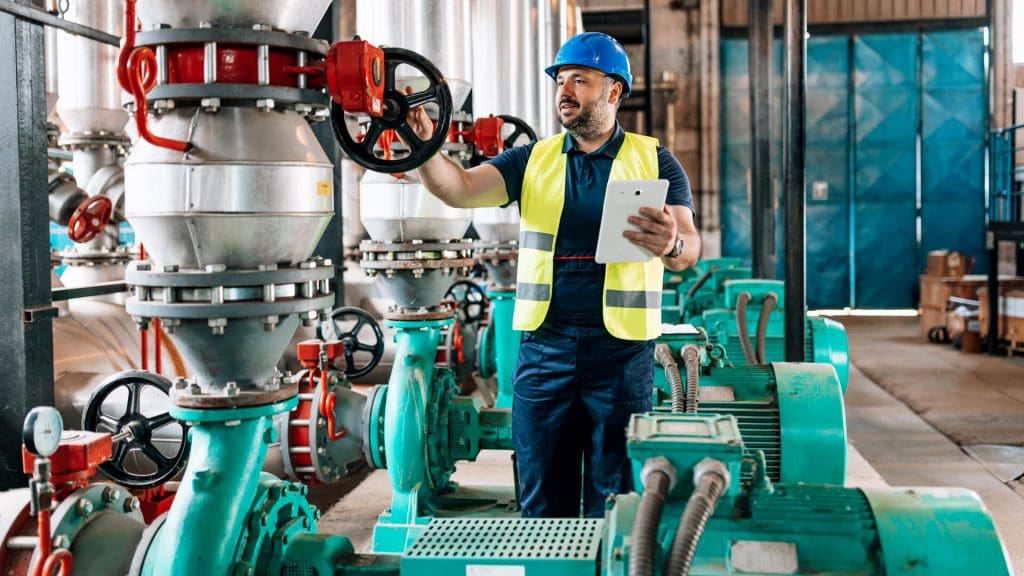 A male engineer is holding his tablet and performing a system check in a heating plant.