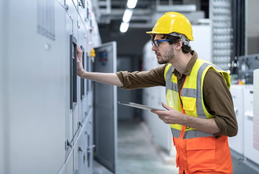 Young Electrician working at electrical room, Industrial service engineer during shutdown checking conducts of control panel note with digital tablet in energy control room at power plant.