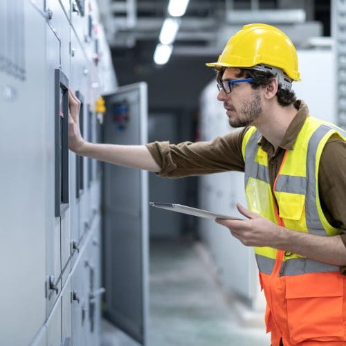 Young Electrician working at electrical room, Industrial service engineer during shutdown checking conducts of control panel note with digital tablet in energy control room at power plant.