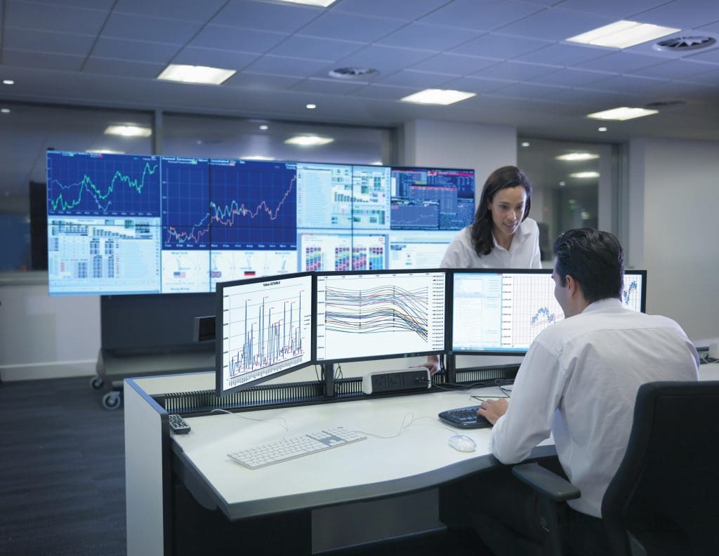 people sitting in front of a bank of monitors with graphs and charts