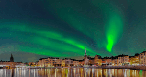Northern lights glowing above a Nordic city skyline, reflecting over the water, symbolizing the Nordic energy transition and renewable innovation.