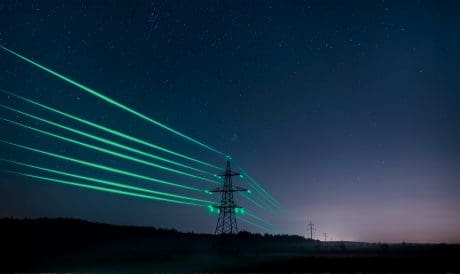 High-voltage transmission tower illuminated with green light beams under a starry night sky, symbolizing the connection between AI and the power grid.